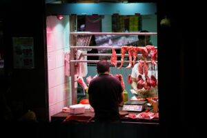 man standing in front of stall with hanged meats